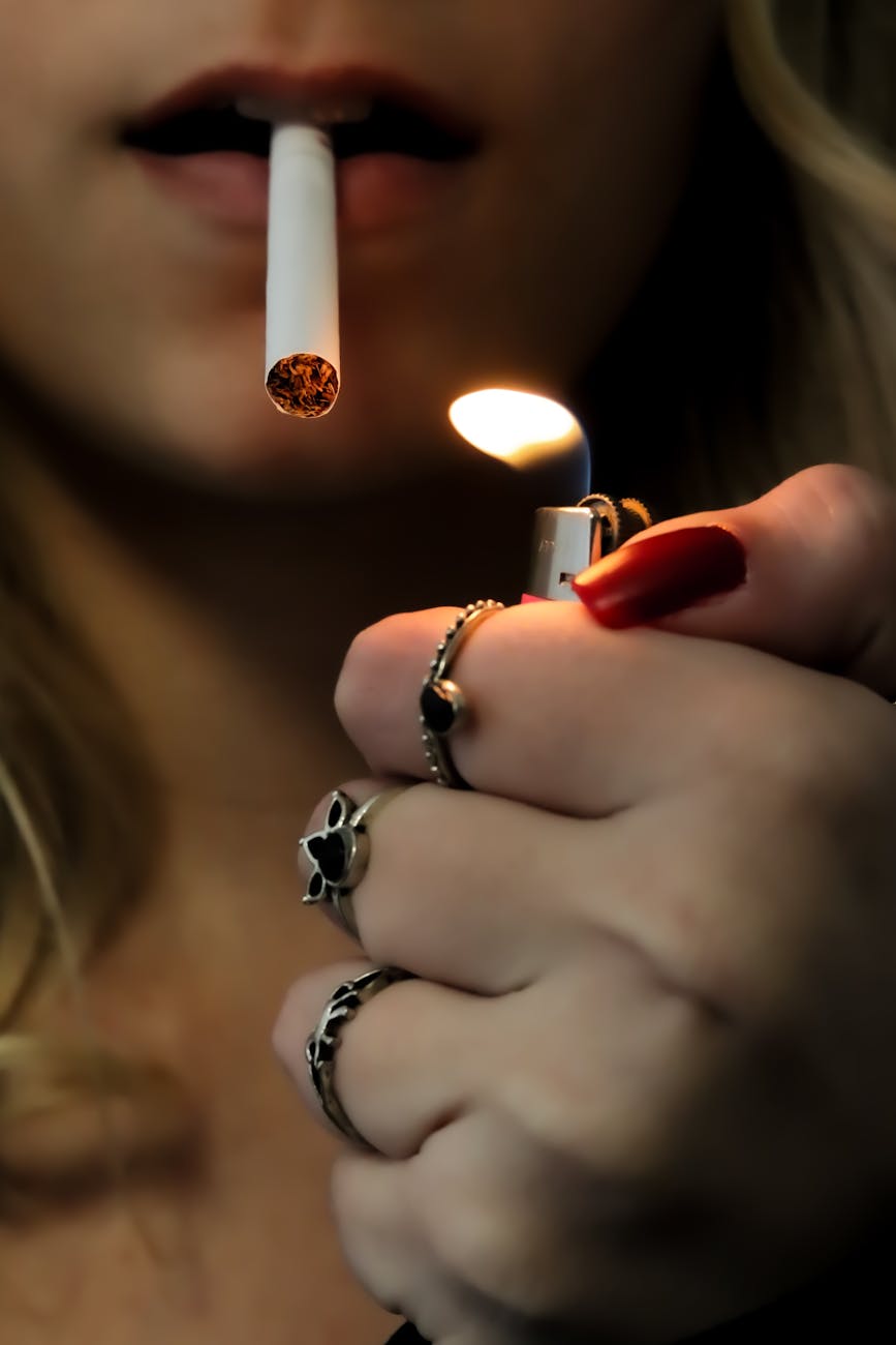 A close-up image of a woman lighting a cigarette, focusing on the flame and rings.